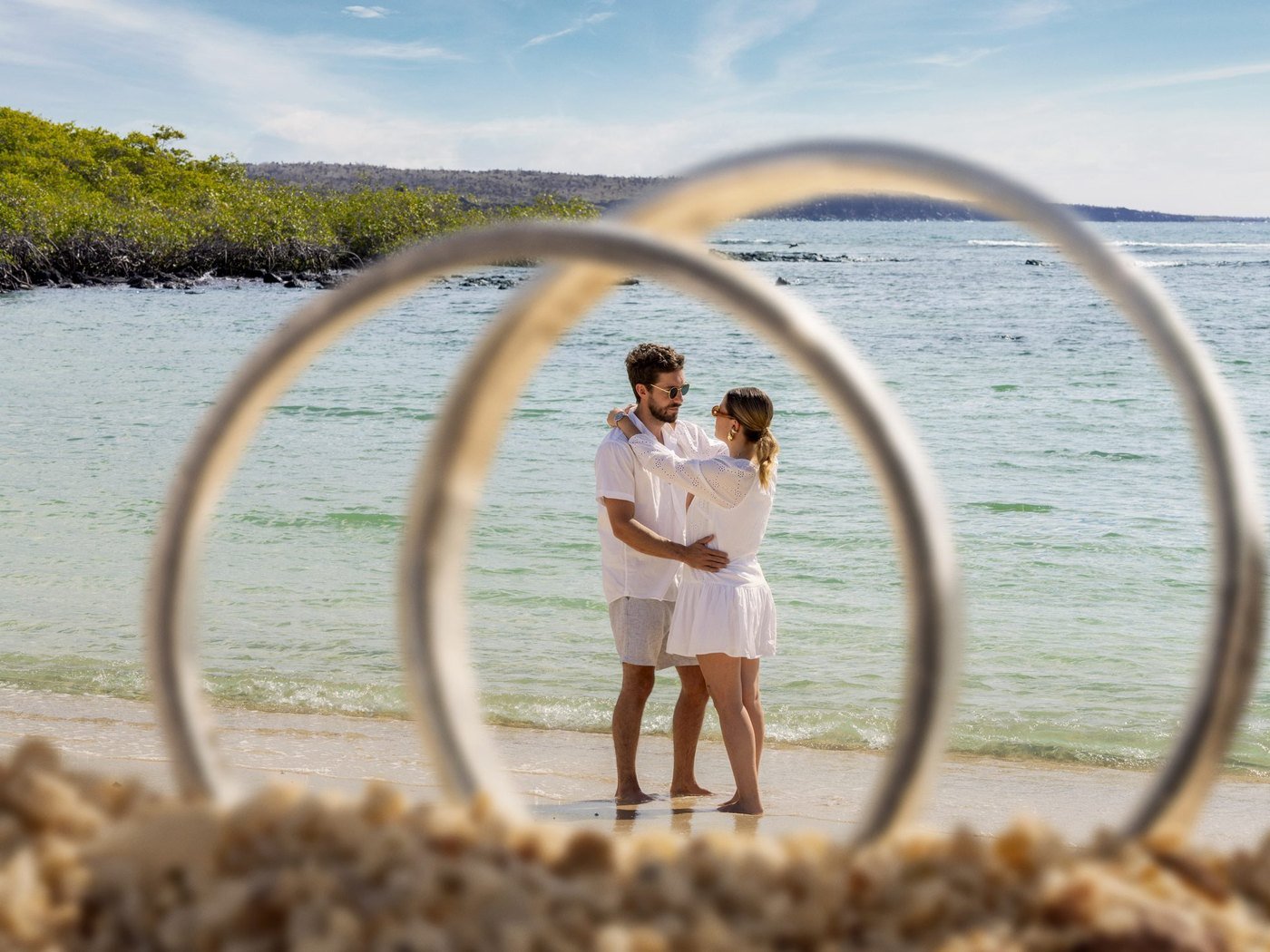 Wedding couple on a Galapagos beach, framed by wedding rings